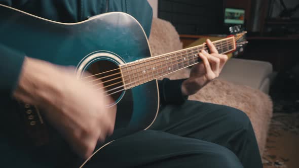 Man Plays an Acoustic Guitar While Sitting on a Couch alt