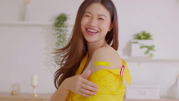 Happy Asian Woman received anti virus vaccine cheerful thumbs up with bandage alt