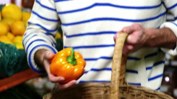 Man with a baskets selecting bell pepper in organic section alt