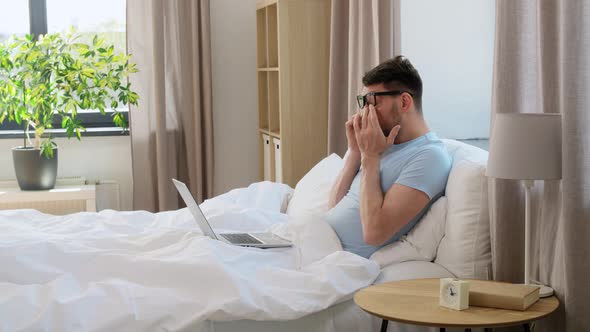 Tired Man in Glasses with Laptop Working in Bed