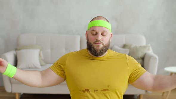 Funny Fat Man Newcomer in Sport Doing Meditation Sitting on Yoga Mat at Home
