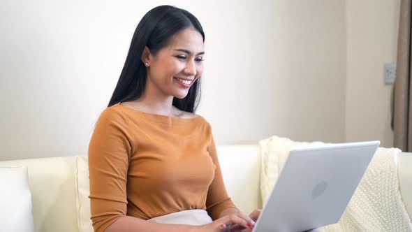 Young woman sitting on sofa using laptop for work at home