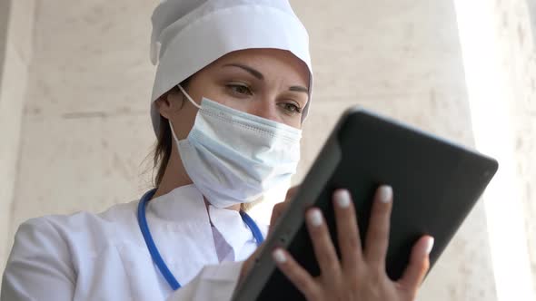 Female Doctor in Medical Mask Is Using a Tablet Computer