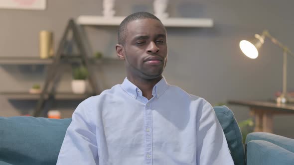 Portrait of African Man Showing NO Sign While Sitting on Sofa alt