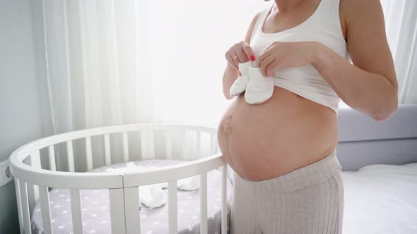 Young Pregnant Woman Small Baby Shoes Sitting Sofa Home alt