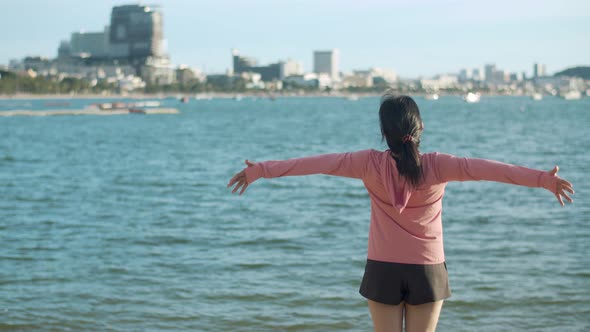 An attractive woman jogging in sportswear raises arms into the air. alt