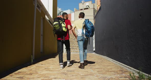Back view of two mixed race male friends walking in the street alt