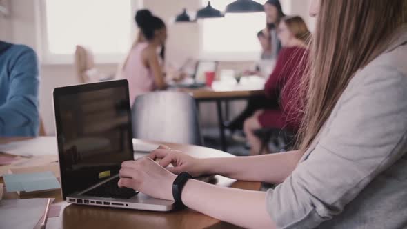 Close-up of Young Female Freelance Worker with Smart Watch Typing on Laptop By the Table in Busy alt
