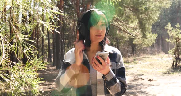 Woman walking in headphone, turns on the smartphone podcast and listening it forest sun shine alt