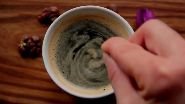 A Man Stirs Sugar in a Cup of Aromatic Coffee. A Cup of Aromatic Coffee Is Placed on a Wooden Table