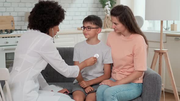 Afro American Woman Doctor Listens to Child's Lungs Using Stethoscope During Checkup alt