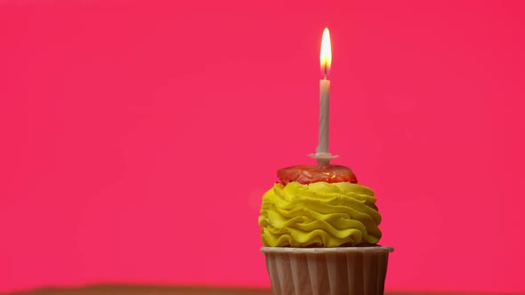 Delicious Festive Cupcake with Yellow Cream with a Burning Candle Spinning on a Light Pink alt