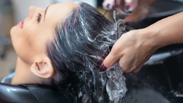 Closeup Caring Hands Female Hairdresser Washing Hair to Brunette Woman Using Professional Shampoo alt