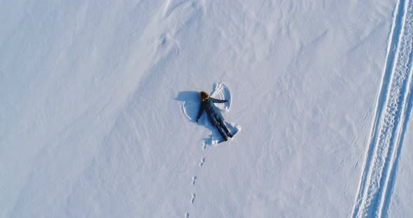 Woman Makes Snow Angel Laying in the Snow. Aerial Video. Camera Moves Away Slowly.