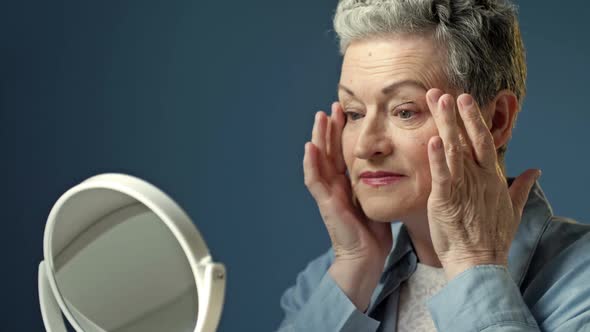 An Elderly Graying Woman Carefully Examines Her Reflection in the Mirror Lightly Touching the