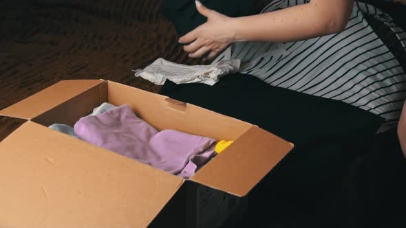 Young Girl Collects a Parcel With Things and Examines Clothes alt