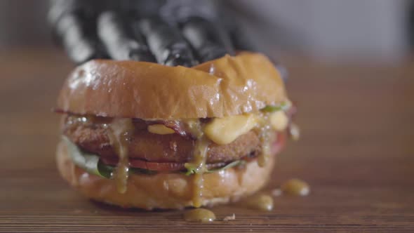 Hand of the Chef in Black Rubber Gloves Pressing Burger and Sauce Flows Out alt