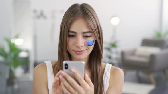 Close-up Portrait of Young Pleasant Woman Texting on Her Phone Sitting at Home alt