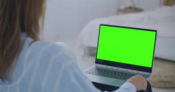 Young Woman at Home Works on a Laptop Computer with Green Mock-up Screen. She Sitting On a Couch in alt