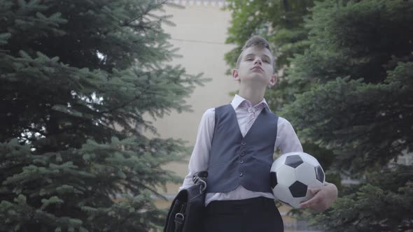 Handsome Well-dressed Boy Standing on the Street Holding the Soccer Ball and Purse alt