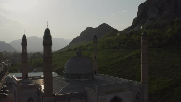 A Beautiful Muslim Mosque in Rays of Sunset Sunlight Against Background of Rocky Mountains and Sky