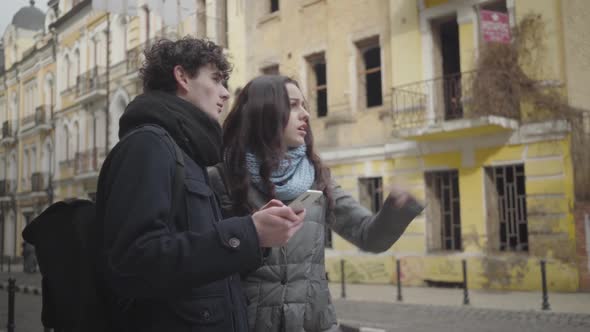Young Caucasian Couple Discussing the Route and Leaving. Boyfriend and Girlfriend Using Online Map alt