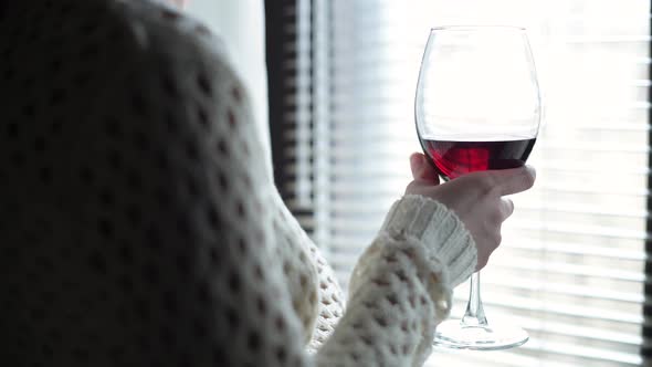 wine glass in the hands of a girl who stands in front of the window. alt