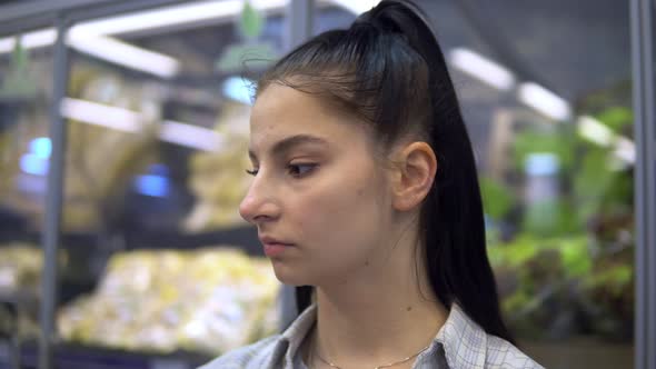 Young Woman in Supermarket Looking on Shelves Choosing Products