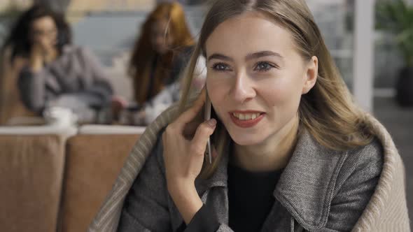 Close-up of Young Caucasian Woman Covered in Blanket Talking By Cell Phone While Sitting at the alt