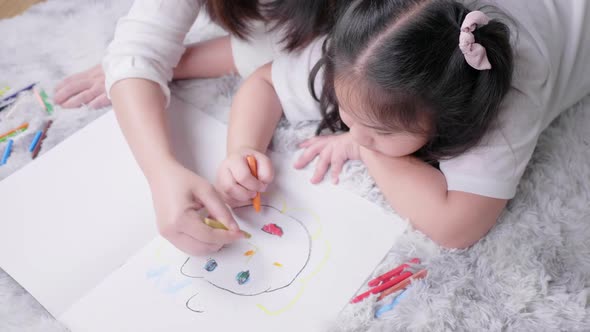 Top view of Asian mom and her kid lying on the floor and drawing on paper together alt