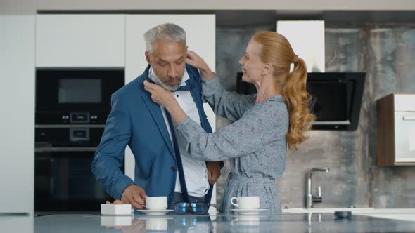 Senior Woman Help Husband with Tie Indoors at Home Kitchen alt