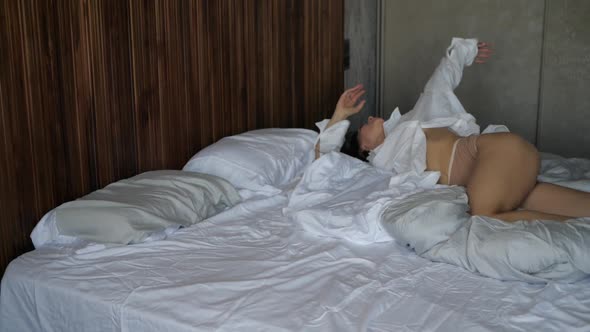 Woman in a Shirt and Bare Legs Lies on a White Bed in a Hotel Room