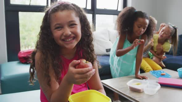 Video of happy biracial girl sitting with friends at school common room and eating alt