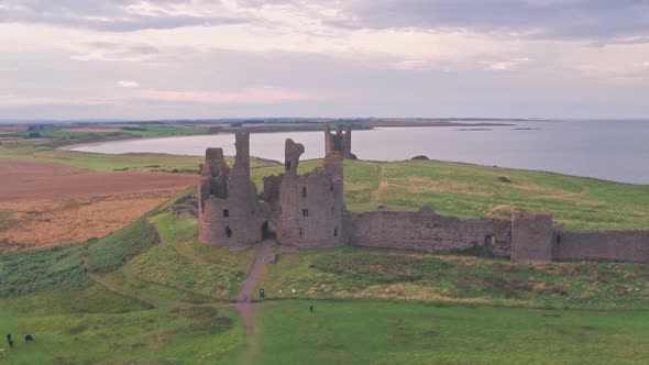 Dunstanburgh Castle at sunset in Northumberland, England, UK, Aerial drone reveal alt
