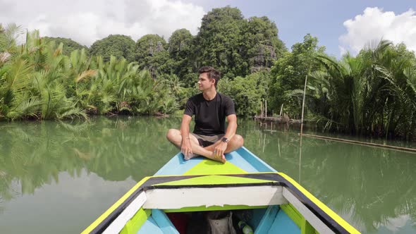 young caucasian man sitting on a boat ride along a river in ramang ramang sulawesi surrounded by man alt