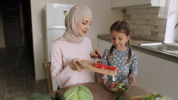 Arabian Mother in Hijab and Cute Little Daughter Throwing Sliced Cucumbers in Glass Bowl alt