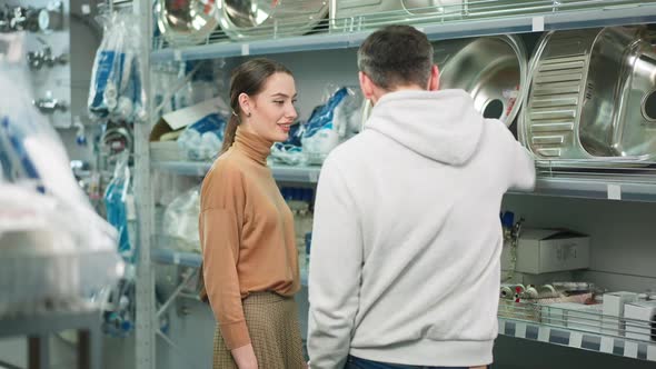 Young Confident Woman Discussing Purchase of New Sink in Hardware Store with Man alt