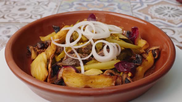 Fried Potatoes with Mushrooms and Onion Rings in Clay Plate Spinning Round on Table