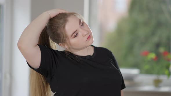 Charming Overweight Caucasian Woman Stretching Neck Exercising at Home in the Morning alt