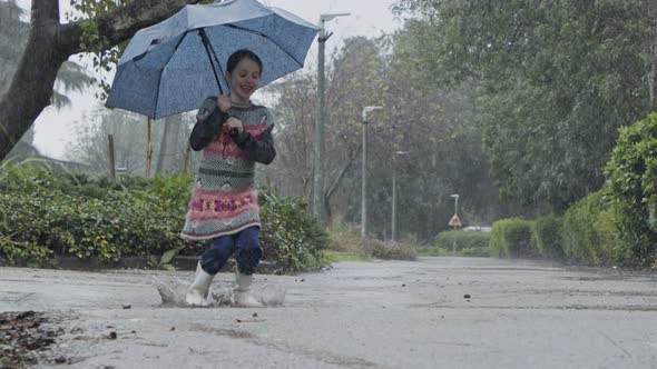 Slow motion of a little girl skipping in puddles holding an umbrella in the rain alt