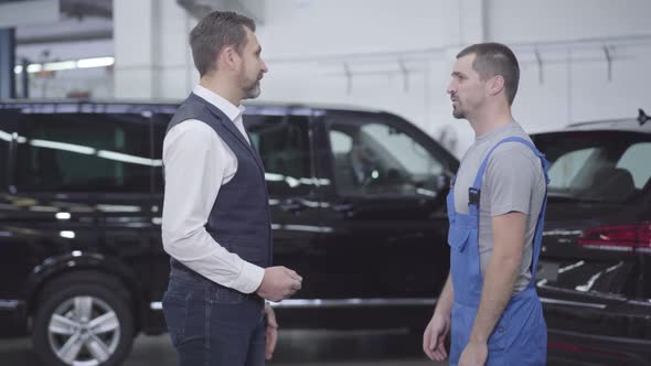 Side View of Two Caucasian Men Standing in Auto Repair Shop and Talking. Successful Businessman alt