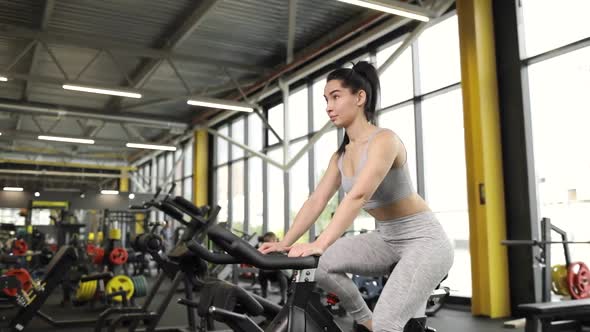 Beautiful Sportive Brunette Woman Doing Cardio on a Exercise Bike at Gym