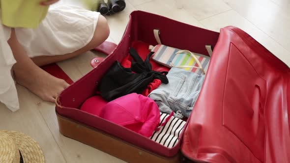 Young girl preparing for vacation. Pack up clothes in suitcase at home. alt