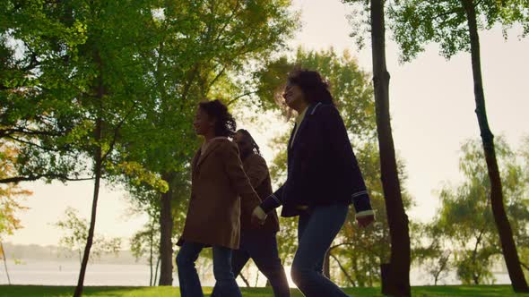 Child Walking Holding Parents Hands in Green Park alt