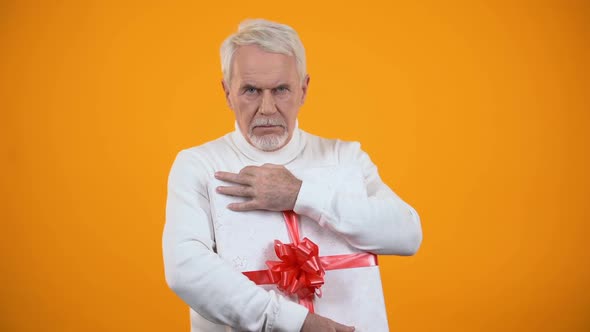 Greedy Male Pensioner Embracing Giftbox and Seriously Looking on Camera, Avarice alt