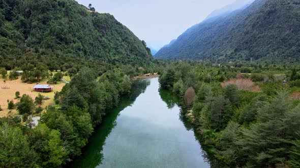 Dolly out aerial view of the Cochamo River and Cochamo Valley with mountains in the background. alt