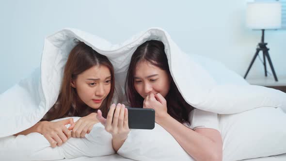 Asian attractive lesbian couple use mobile phone watch movie on bed. alt