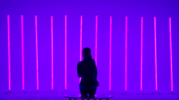 Dark Silhouette of a Gymnast Against the Background of Multicolored Neon Lamps alt