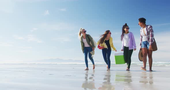 Happy group of diverse female friends having fun, walking along beach alt