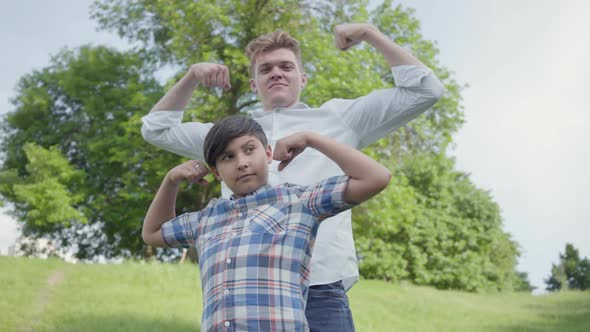 Portrait Cute Young Father and Adorable Boy Showing Muscles Looking Into the Camera Outdoors. Father alt